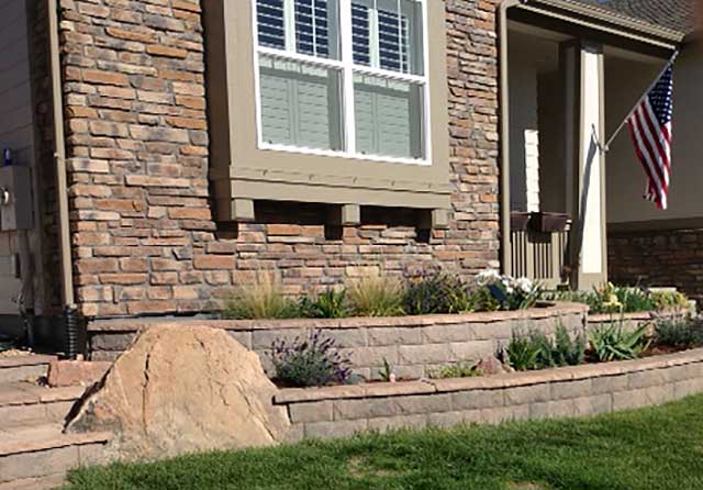 This entryway planter treatment in Berthoud uses stone retaining walls with red flagstone finishes to create the planter, along with natural boulders for accent.